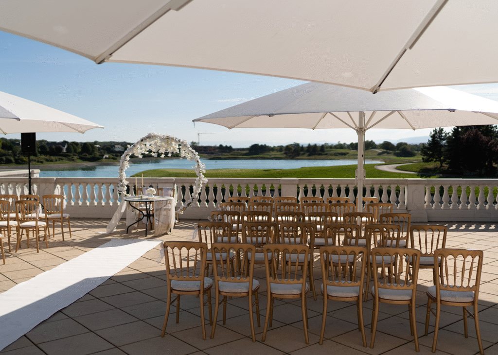 A wedding venue set on a high rise above a lake with umbrellas shading the chairs.