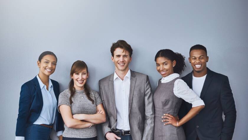 Group of people in corporate attire standing against a blank background and smiling.