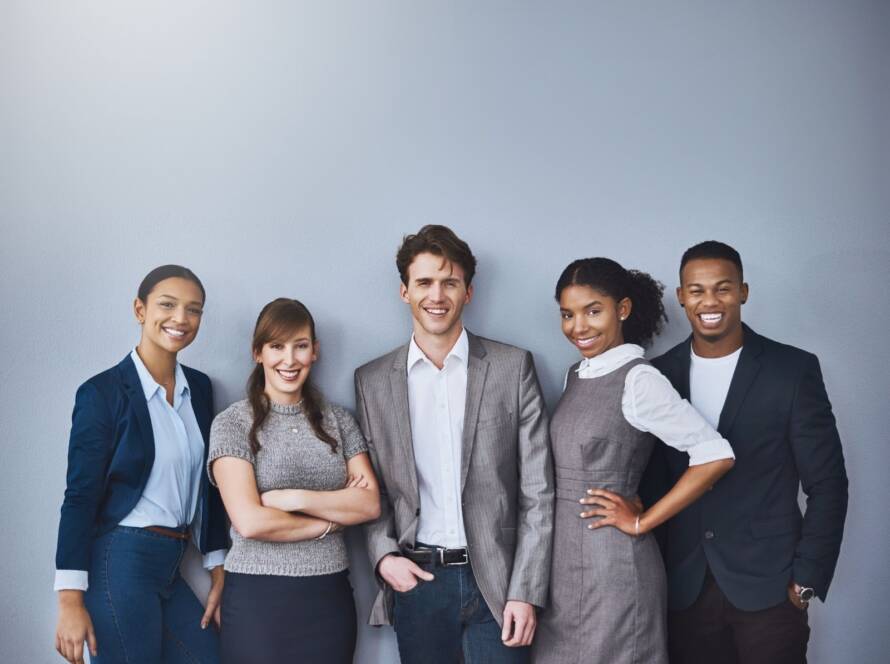 Group of people in corporate attire standing against a blank background and smiling.