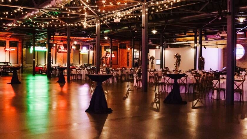 A large rental venue with classic cars, tables high and low, and hanging lights. 