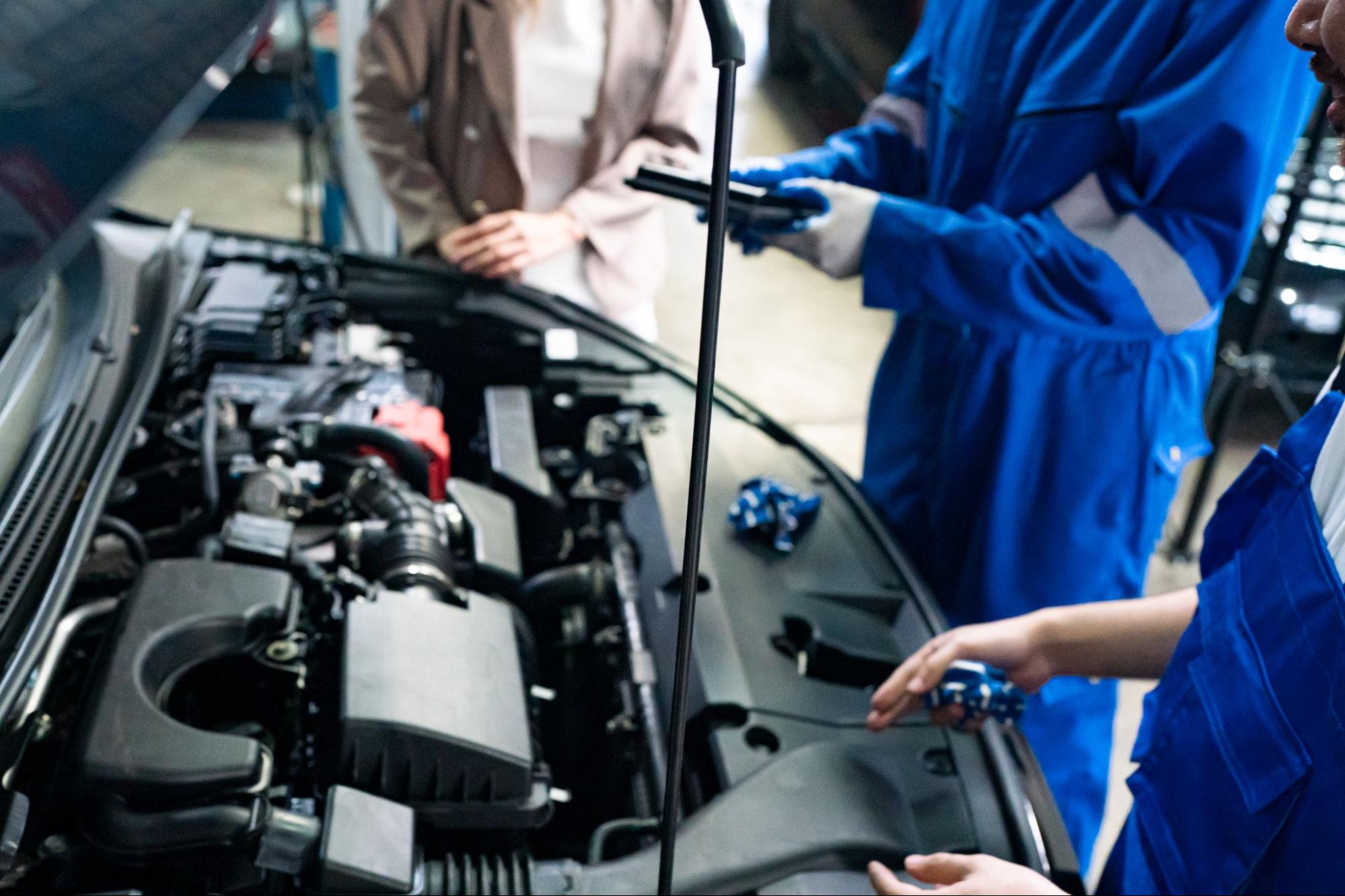 Mechanics in blue overalls inspecting a car engine during maintenance.