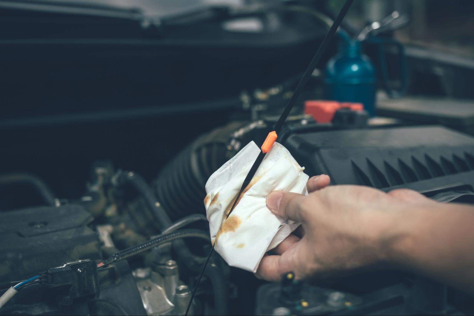 Car mechanic checking engine oil with a dipstick and wiping it clean with a tissue